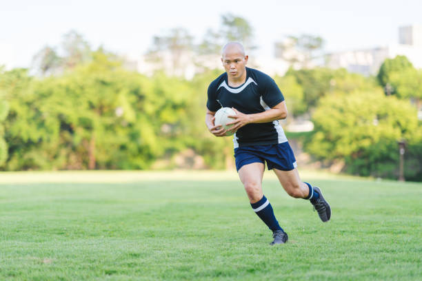 A rugby player is holding a rugby ball and running.