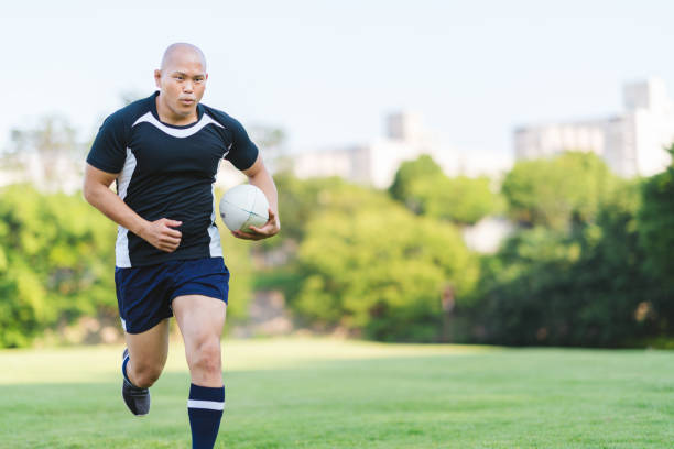Rugby player holding rugby ball and running A rugby player is holding a rugby ball and running. skin head stock pictures, royalty-free photos & images