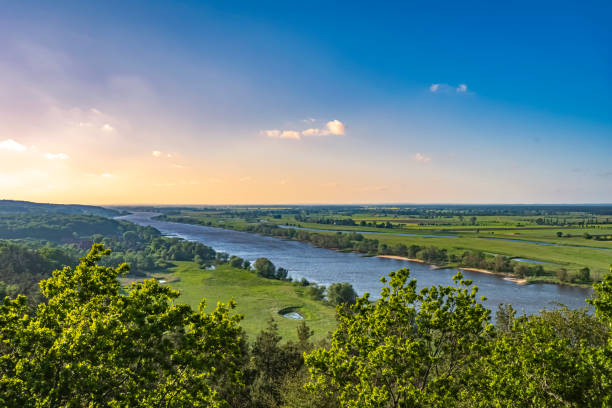 View over the Elbauen in Lower Saxony, Germany. You see a landscape with fields, meadows and the river Elbe under a blue sky with clouds, which are illuminated by the sun.