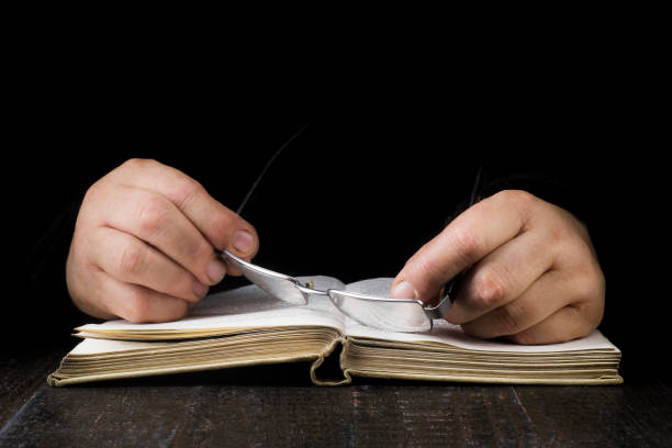 istock An open book on which someone put his hands with glasses 1166845990