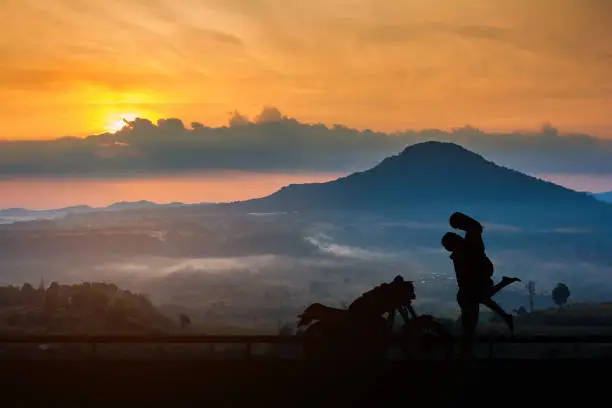 Photo of Couple silhouette kissing at sunset and have a big bike parked on the street,enjoying freedom and active lifestyle, having fun on a bikers tour on sunset background.