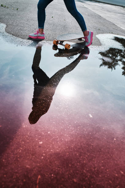 istock Puddle reflection of a girl riding on longboard. 1166857904