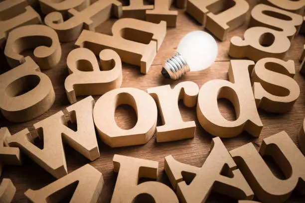 Words alphabets in scettered wood letters on the table with glowing light bulb as communication idea or words have power concept