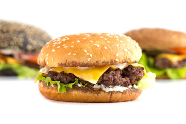 istock Big burger close up on a white background. Beef patty burger, cheddar cheese, lettuce, bacon, pickled cucumber, tomato and balsamic sauce. In the background are two burgers. 1166860913