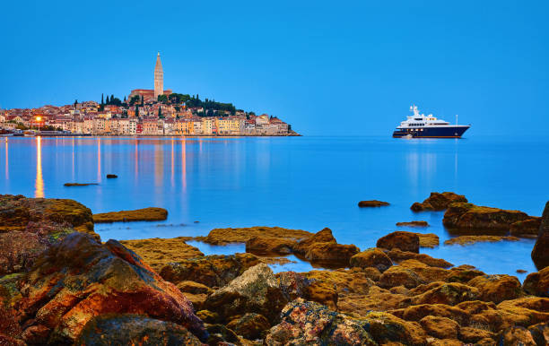 Rovinj, Croatia. Antique medieval old town nighttime view. Luxury yacht and fishing sea. Big stones Rovinj, Istria, Croatia. Antique medieval old town at Adriatic sea. Calm summer morning with blue sky. Panorama with nighttime illumination. View at chapel of Church of Saint Euphemia. Luxury yacht yacht rock music stock pictures, royalty-free photos & images