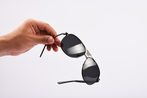 Male hand holding sunglasses on white background