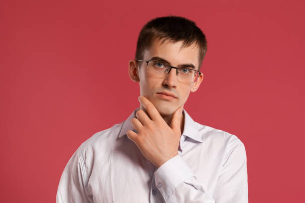 istock Young man in a classic white shirt is posing over a pink background 1166866516