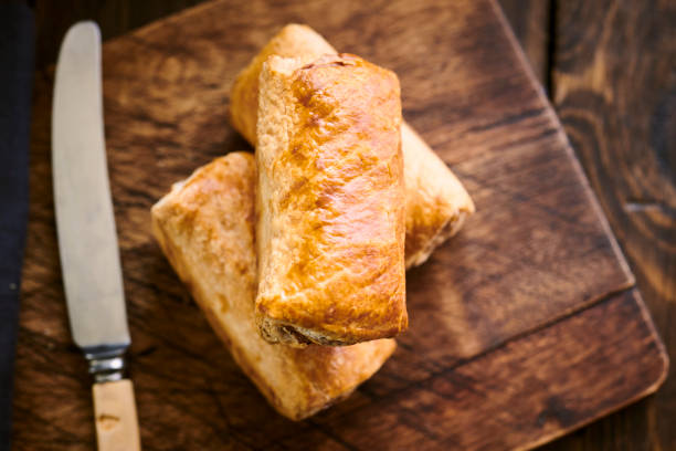 Three sausage rolls arranged on a rustic wood chopping board. Three sausage rolls arranged on a rustic wood chopping board. sausage roll stock pictures, royalty-free photos & images