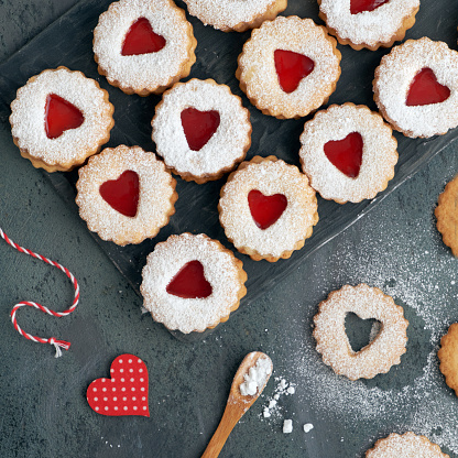 Top view of traditional Linzer cookies with red jam heart on dark background. Christmas or Valentine traditional tasty snack.