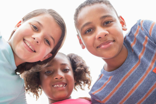 Multi-ethnic group of school children friends in huddle. Multi-ethnic, mixed age group of school children, friends huddle overhead. The group of friends huddle up to plan their next adventure. Back to school, education themes. boy and girl looking at camera stock pictures, royalty-free photos & images