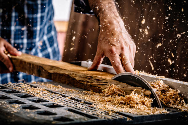 Male Hispanic carpenter using saw in home workshop with wood chips flying and protective eyewear