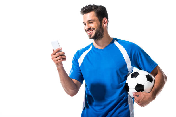 joueur de football de sourire avec la bille utilisant le smartphone d'isolement sur le blanc - soccer player soccer men smiling photos et images de collection