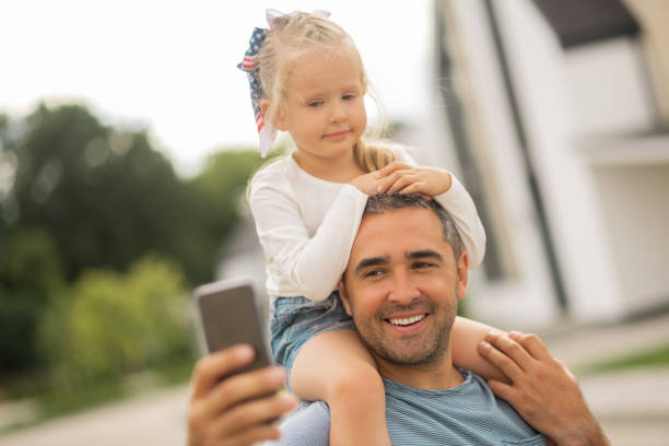 istock Cute girl looking into camera while father making selfie 1166883102