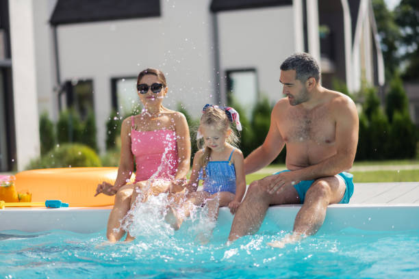 istock Daughter splashing water while sitting near pool with parents 1166883830