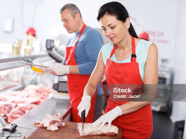 Portrait Of A Female Butcher Cutting A Piece Of Meat In Butchers