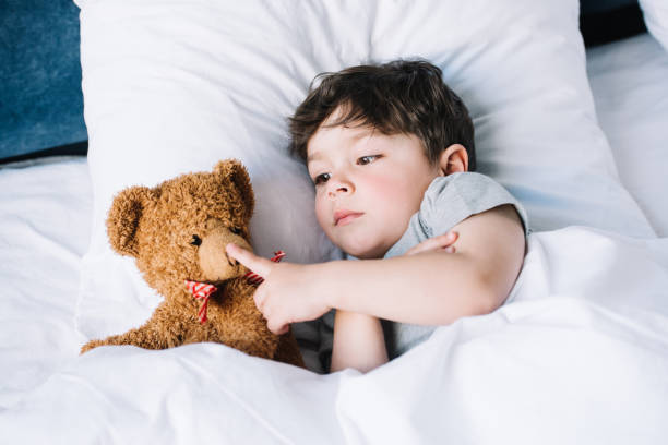 istock adorable kid lying on white pillow and touching teddy bear at home 1166888629