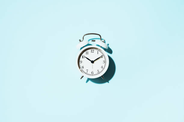 istock White alarm clock with hard shadow on blue background. Top view 1166889624