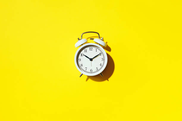 istock White alarm clock with hard shadow on yellow background. Top view. Wake up alert concept. Morning routine. 1166889628