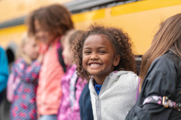 istock Happy student stands with her friends next to a school bus 1166891911