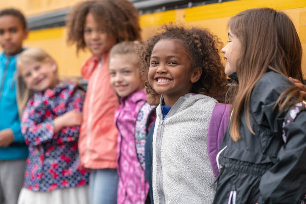istock Happy student stands with her friends next to a school bus 1166891924