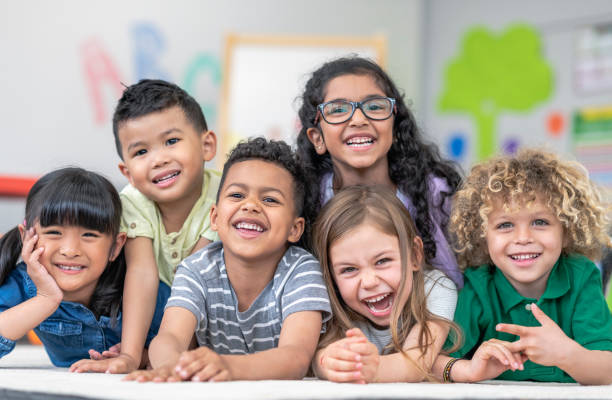 Group of smiling students Portrait of a happy multi-ethnic group of kindergarten age students. The cute children are laying in a pile on the ground in a modern classroom. The kids are laughing and smiling. montessori education photos stock pictures, royalty-free photos & images