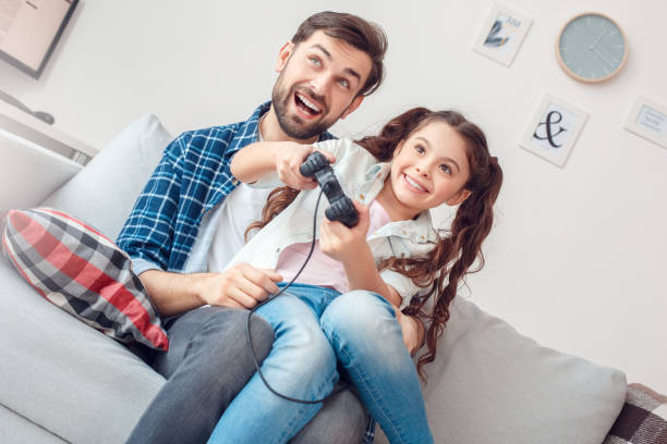 istock Father and little daughter at home sitting holding controller playing happy 1166900336