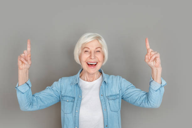 istock Senior woman in jeans jacket studio isolated on grey wall pointing up link 1166900477