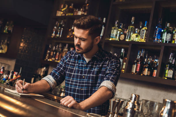 istock Young bartender standing at bar counter writing receipt concentrated 1166902897