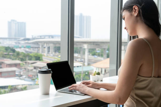 istock Young business woman using laptop computer while sitting at cafe table next to office windows. 1166919277