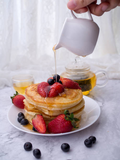 istock Close up hand pour honey on the pancakes, which are on top with raspberry strawberries.Stack of pancakes with topping.Placed in a white plate on a marble table and copy space 1166922504