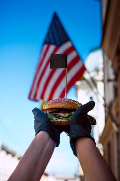 istock burger in hand on american flag background 1166926291