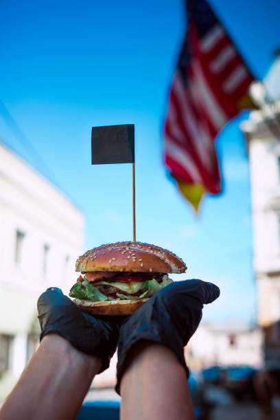 istock burger in hand on american flag background 1166928832