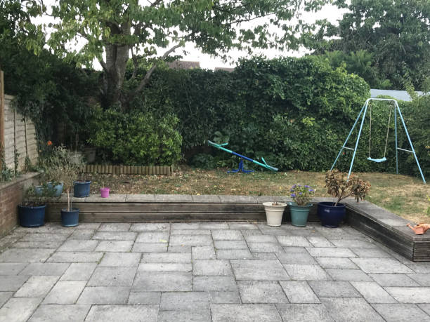 image of modern back garden design yard with zigzag raised lawn and large irregular patio paving slabs outside house in summer with children's playground equipment to play on seesaw and swing, on dead lawn grass turf needing water weed feed after drought - construction platform wood nature contemporary imagens e fotografias de stock