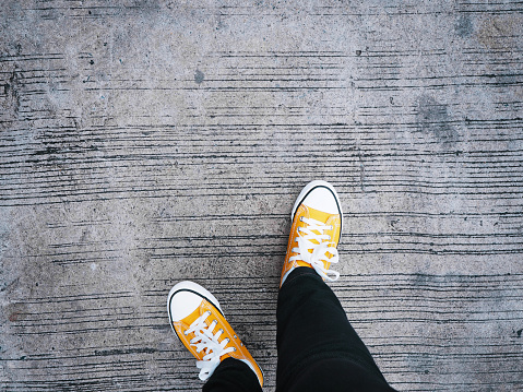 Selfie above view feet wearing yellow sneakers moving on concrete road.