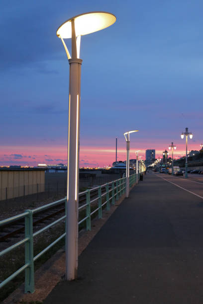 Image of modern metal street lamps lights at night with deep midnight blue sky and salmon pink red sunset by Brighton beach pier, seaside holiday photo of stunning sunset sunrise with contemporary lighting and pavement railings, beachfront promenade Stock photo of modern metal street lamps lights at night with deep midnight blue sky and salmon pink red sunset by Brighton beach pier, seaside holiday photo of stunning sunset sunrise with contemporary lighting and pavement railings, beachfront promenade pavement ends sign stock pictures, royalty-free photos & images