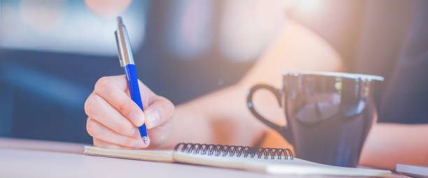 istock Woman hand is writing on a notebook with a pen in office.Web banner. 1166932931