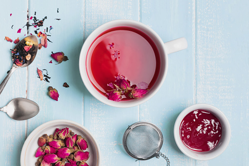 Herbal tea and dry roses on blue colored table, top view