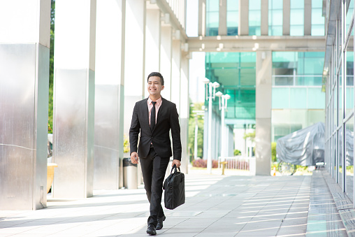 Businessman with suitcase walking outside office building.