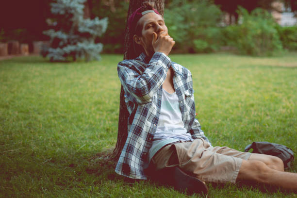 young male sleeping in the public park on the grass under the tree