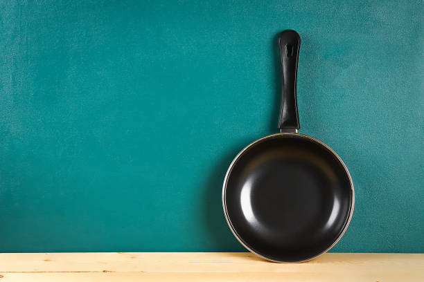 black frying pan on a wooden shelf on teal background. kitchenware. - pan frying pan fried saucepan imagens e fotografias de stock