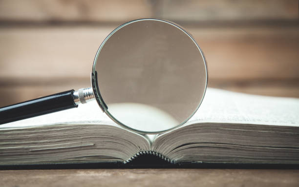 istock Magnifying glass with book on a wooden table. Search and discover 1166949730