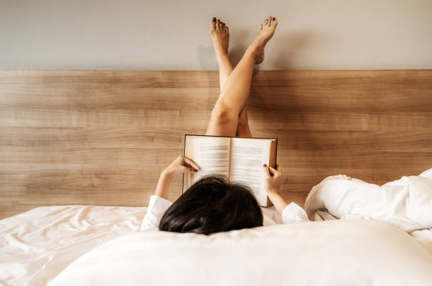 Asian woman lying down, legs crossed, she was reading a book on the bed stock photo