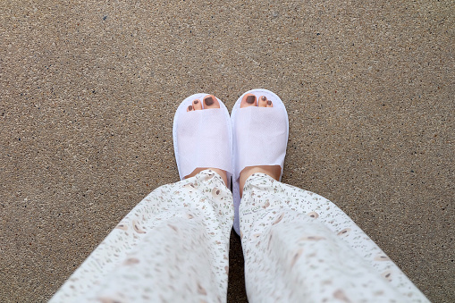 Selfie slippers on concrete background, Top view. Beautiful young woman wearing white slipper and pants. Clear warm domestic sandal. Soft comfortable bed shoes accessory footwear.