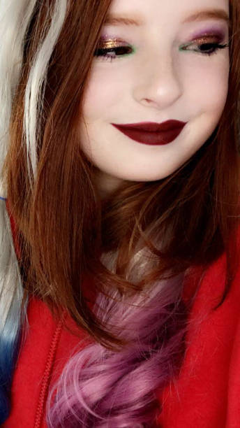 ●赤毛の十代の少女14/15歳の赤い筋のかつらを着た笑顔のイメージ、赤い口紅、ジョーカー風の唇とゴールドのキラキラアイシャドウでフルフェイスメイク - teenage girls 14 15 years women human face ストックフォトと画像