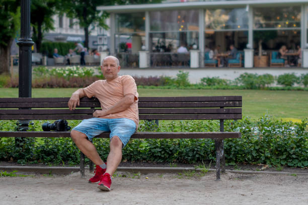 A middle age man sits on a bench in a park.
