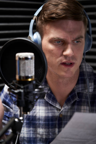 istock Voiceover Artist In Recording Studio Reading From Script Into Microphone 1166981105