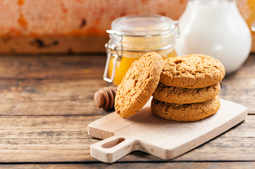 Oatmeal cookies with milk and honey on a wooden background.