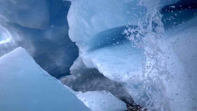 Melting of a glacier. Interior of an ice cave. Water flowing down from above with splashes. Slow motion shot