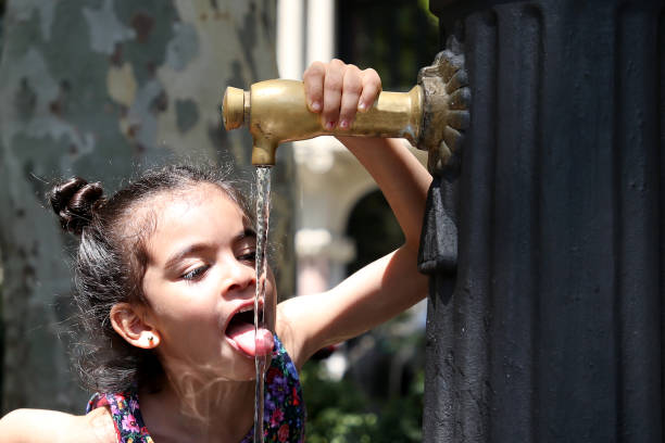 A Muslim preschooler girl drinking water from running pipe.