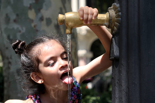 A Muslim preschooler girl drinking water from running pipe.